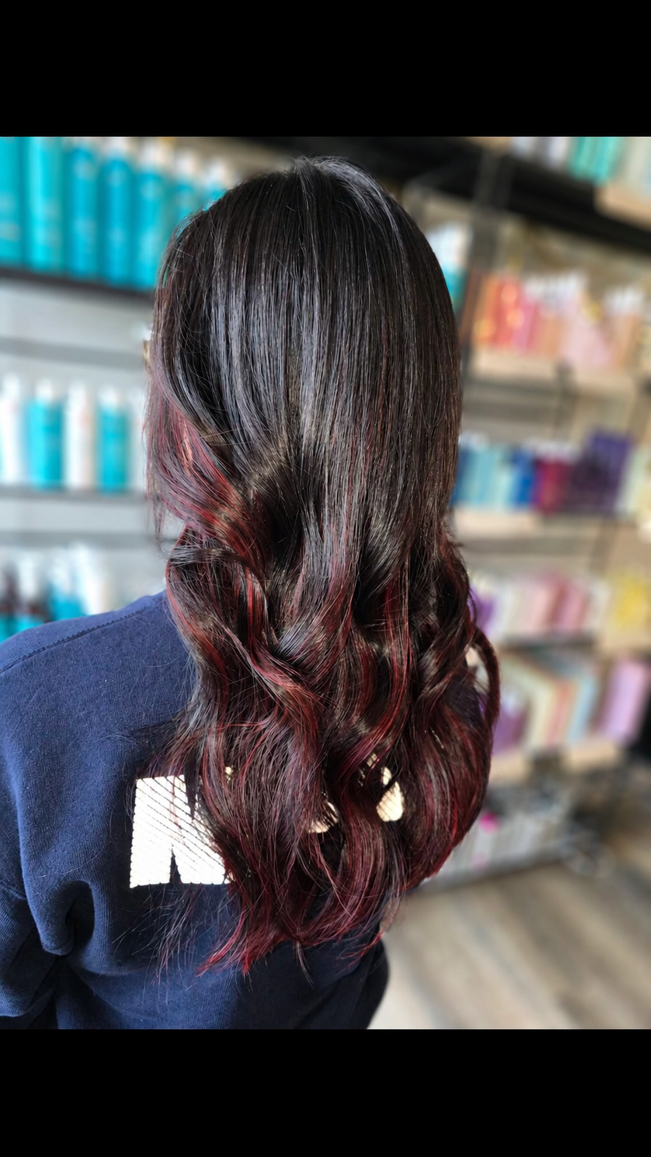 Dark hair with subtle red peekaboo highlights, long wavy style